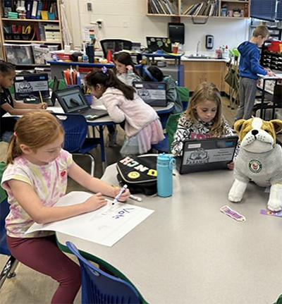 Students sitting at a round table with stuffed animal mascot