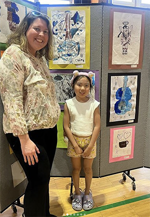 A teacher and a little girl in front of artworks on wall