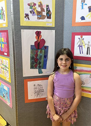 Little girl dressed in purple shirt and shorts in front of artworks on wall