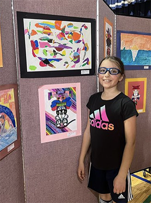 Little girl dressed in black tee shirt and shorts in front of artworks on wall