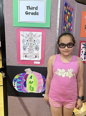 Little girl dressed in pink tee shirt and shorts in front of artworks on wall